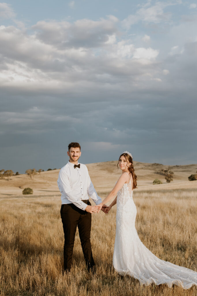 Charles and Ishana posed in a field against a stormy sky on their wedding day at The Hayshed by Meredith Photography