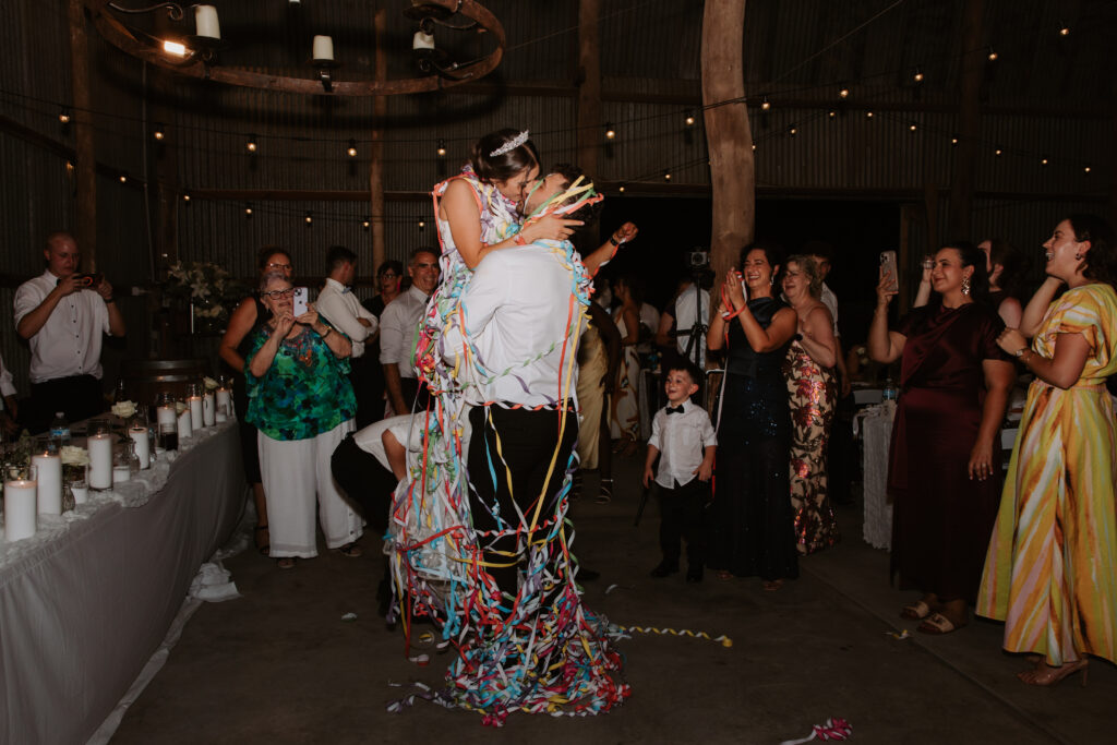 Couple kiss on the dancefloor at The Hayshed wraped in streamers, an italian tradition Shot by Meredith Photography