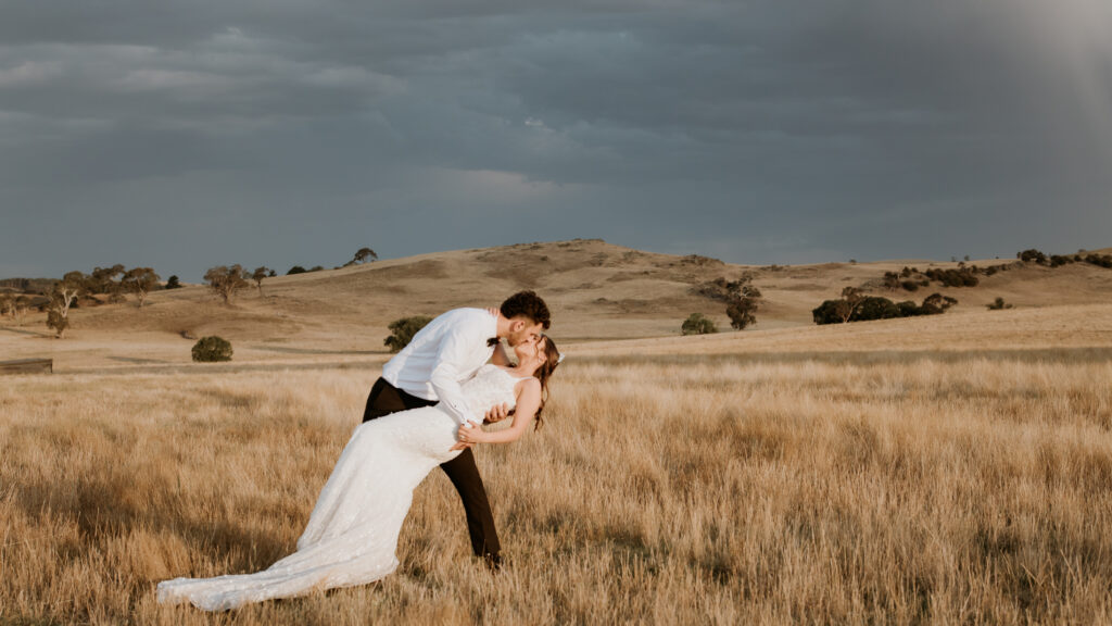 Wedding couple in a dip kiss at The Hayshed with rolling countryside shot by Meredith Photography Bathurst and Central West Wedding Photographer